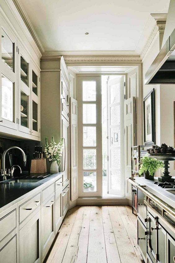 a traditional galley kitchen with vintage dark cabinets, a wooden floor, an access to the balcony with much natural light