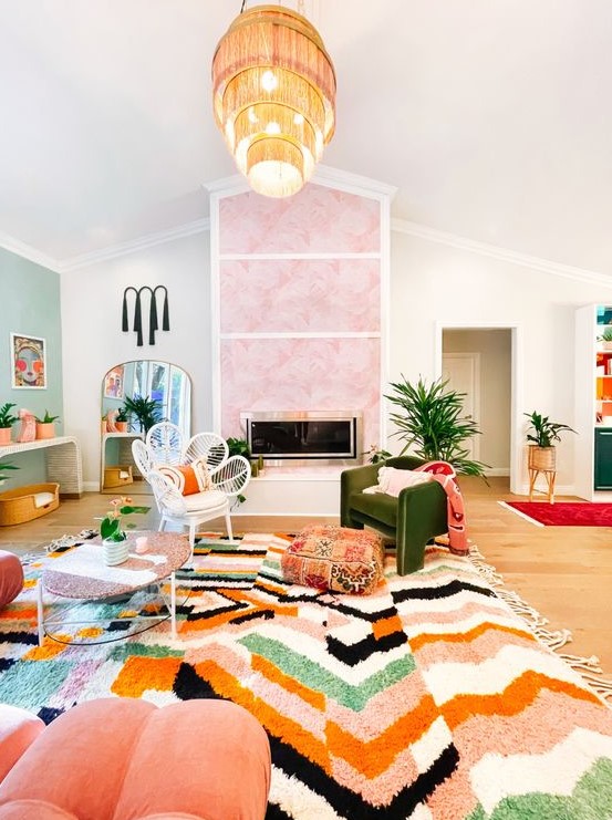 A vibrant maximalist living room with a pink clad fireplace, a green accent wall, a bold bold printed rug, coral furniture and a tiered fringe chandelier.