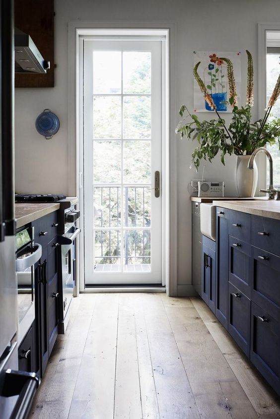 a welcoming navy galley kitchen with wooden countertops, a wooden floor and much natural light coming through the door