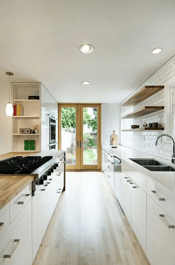 a white galley kitchen with a white subway tile backsplash, open shelves instead of upper cabinets and some lights