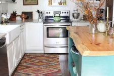 a white traditional kitchen, a colorful boho rug, a blue kitchen island with a wooden countertop with a living edge
