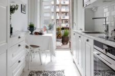 an airy white Scandinavian kitchen with white cabinets, a small dining space by the balcony and a printed rug