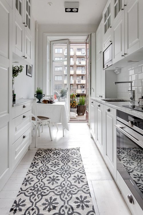 an airy white Scandinavian kitchen with white cabinets, a small dining space by the balcony and a printed rug