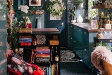 an eclectic and maximalist kitchen with dark wallpaper, teal cabinets, a black bookcase, some shelves and greenery plus a bold rug
