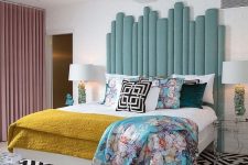 an eclectic bedroom with a bed and an extended aqua headboard, bright bedding, a geometric rug, matching nightstands and lamps
