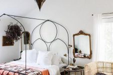 an eclectic bedroom with a metal bed and bright bedding and a bold rug, a rattan loveseat, a Moroccan lamp and mirrors