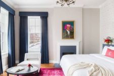 an eclectic bedroom with a navy fireplace, a navy bed with white bedding, a fuchsia rug, navy curtains and white chairs