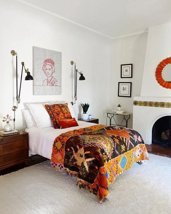 An eclectic bedroom with a vintage hearth with tiles, a bed with colorful bedding, dark stained nightstands, black sconces and potted plants