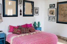 an eclectic bedroom with a wallpaper ceiling, a boho rug and bedding with pompoms, a variety of artworks and retro nightstands