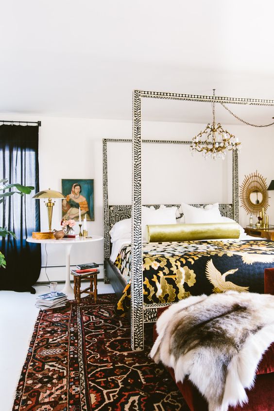 An eclectic bedroom with an eye catchy frame bed, a bold rug, mismatching nightstands and a vintage chandelier