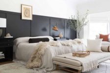 an eclectic bedroom with black paneling, a neutral bed with neutral bedding, a daybed with pillows, a potted tree and a black chandelier