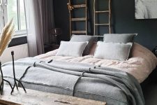 an eclectic bedroom with black walls, a bed with grey and pink bedding, stained benches, ladders and an industrial lamp