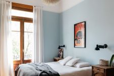 an eclectic bedroom with blue walls, dark-stained nightstands, bold artwork, a fluffy pendant lamp