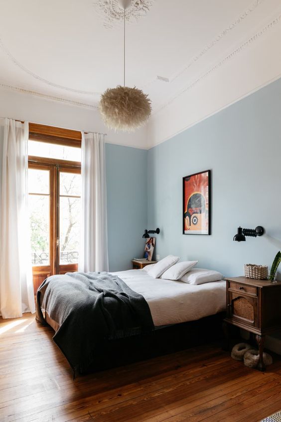 An eclectic bedroom with blue walls, dark stained nightstands, bold artwork, a fluffy pendant lamp
