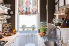 an eclectic galley kitchen with black walls, a checked floor, white cabinets with butcher block countertops and a colorful curtain