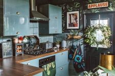 an eclectic kitchen with black walls, blue sleek cabinets, butcherblock countertops, a black and white tile floor and potted plants