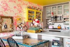 an eclectic kitchen with bold pink wallpaper, a yellow cabinet and a ceiling, a white kitchen island, book stacks, a pink chandelier, a leopard table and stained chairs