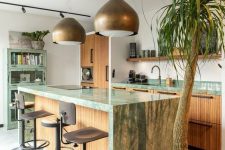 an eclectic kitchen with fluted cabinets and green marble countertops, a shabby chic green storage unit, brass pendant lamps and stools