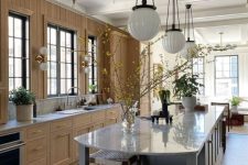an eclectic kitchen with stained cabinets and walls, a grey kitchen island, woven stools, pendant lamps and potted plants