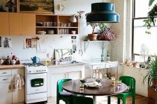 an eclectic kitchen with yellow and white cabinets, retro appliances, a round table, green chairs and a black pendant lamp