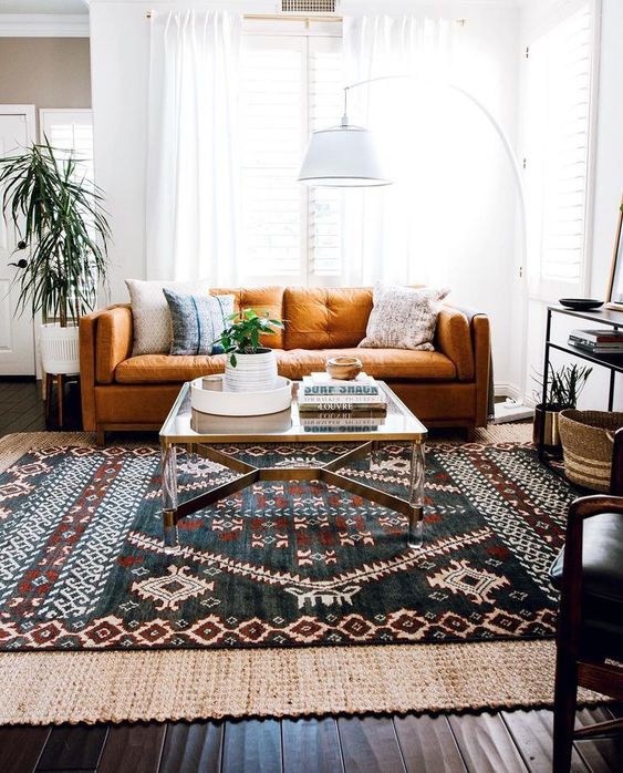 An eclectic living area with a folksy rug, a floor lamp, a rust colored sofa and baskets for storage