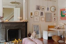 an eclectic living room with a black fireplace, a mirror, a gallery wall, a pink sofa and ottoman, some chairs and candles