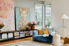 an eclectic living room with a blue and mustard chair, a beige sofa, colorful pillows, a bookshelf, a marble table and artwork