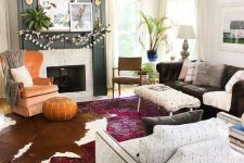 an eclectic living room with a fireplace, a black sofa, a printed chair, an orange one, a leather pouf, a cotton garland and potted greenery