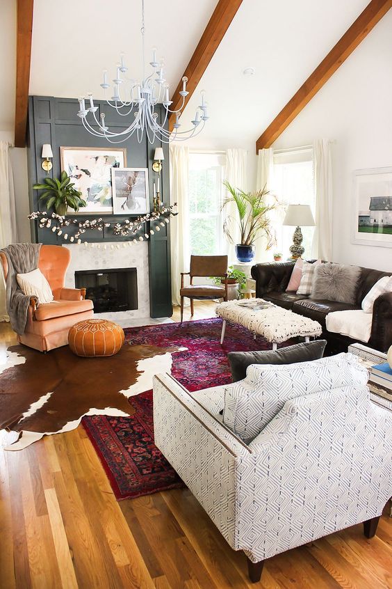 an eclectic living room with a fireplace, a black sofa, a printed chair, an orange one, a leather pouf, a cotton garland and potted greenery