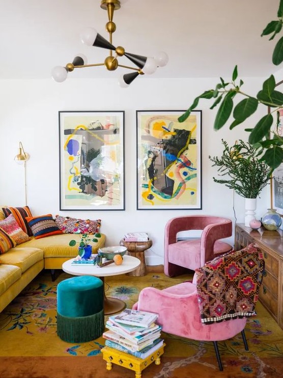 An eclectic living room with a yellow sofa and bright pillows, a bold printed rug, pink chairs, a colorful mini gallery wall and a stack of books.