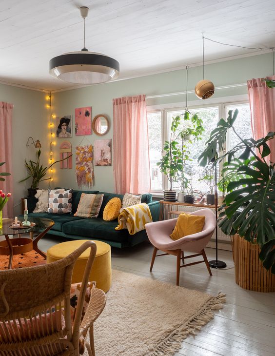 A stylish eclectic living room featuring mint walls, a dark green sofa, and a pink chair. The yellow ottoman adds a pop of color. A bright gallery wall and lights complete this vibrant and artistic space.