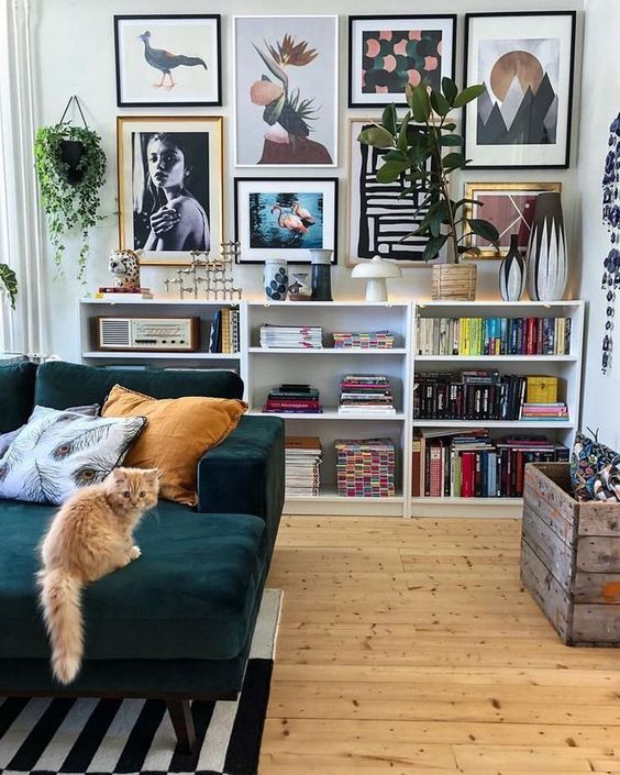 An eclectic living room with open box shelves, a crazy gallery wall, an emrald sof and a striped rug.