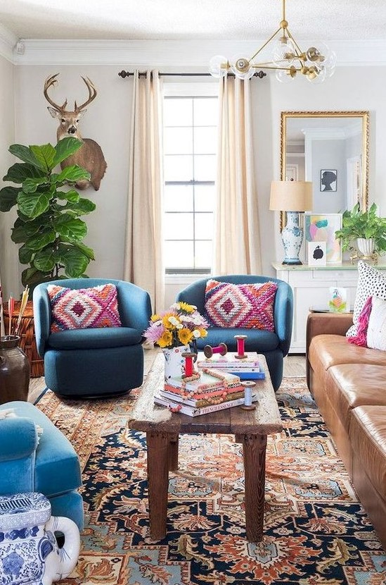 an eclectic space with folksy and boho textiles, a mid century modern chandelier, a leather sofa and bright blue chairs