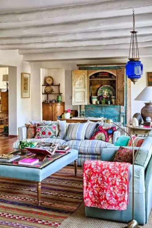 An ethnic maximalist living room with pastel blue seating furniture, a turquoise buffet, a Moroccan lamp and bold ethnic textiles.