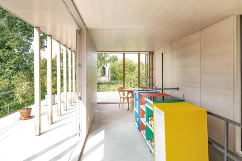 The kitchen is done with light-colored plywood and a row of colorful cabinets that feature storage