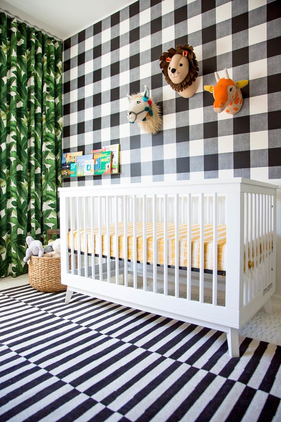 a fun tropical nursery with a mix of prints - a plaid statement wall, a striped rug and a tropical leaf print curtain