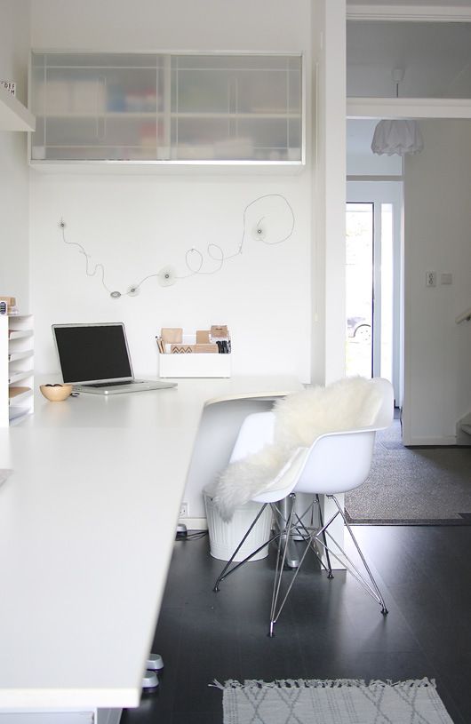 A minimalist white home office with a long and sleek desk, some wall mounted cabinets and a comfy chair