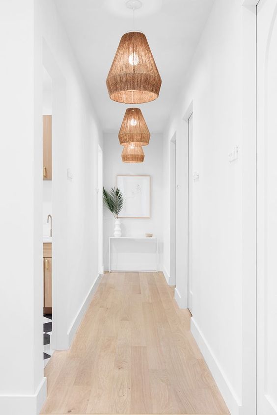 a white long and narrow hallway is done with wicker pendant lamps and tropical leaves to highlight the ambience