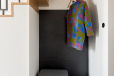 06 The tiny entryway nook is clad with black tiles, an upholstered seat with storage space and a clothes holder