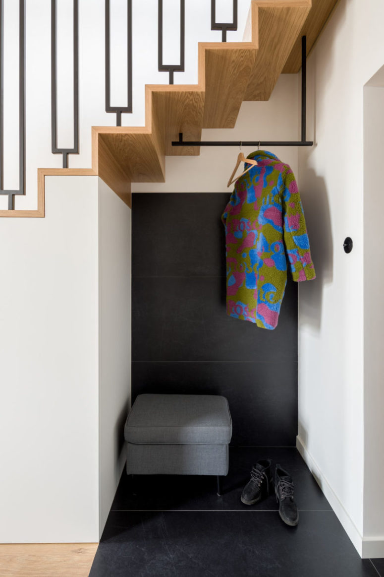 The tiny entryway nook is clad with black tiles, an upholstered seat with storage space and a clothes holder