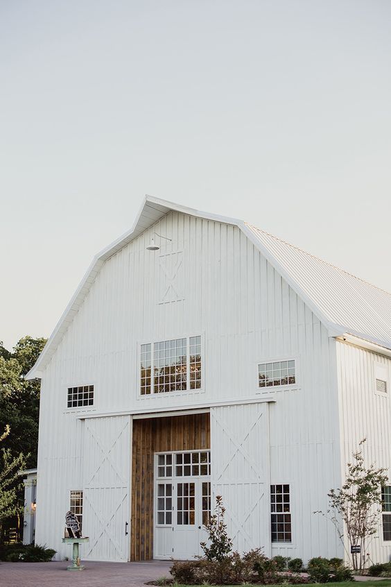 a beautiful white barndominium with stained wood and sliding doors that cover the entrance