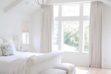 06 a very fresh white bedroom with creamy curtains and stools, an elegant chandelier and a white upholstered bed