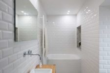07 The bathroom is fully done in white, with chic tiles, a wooden vanity and a built-in bathtub