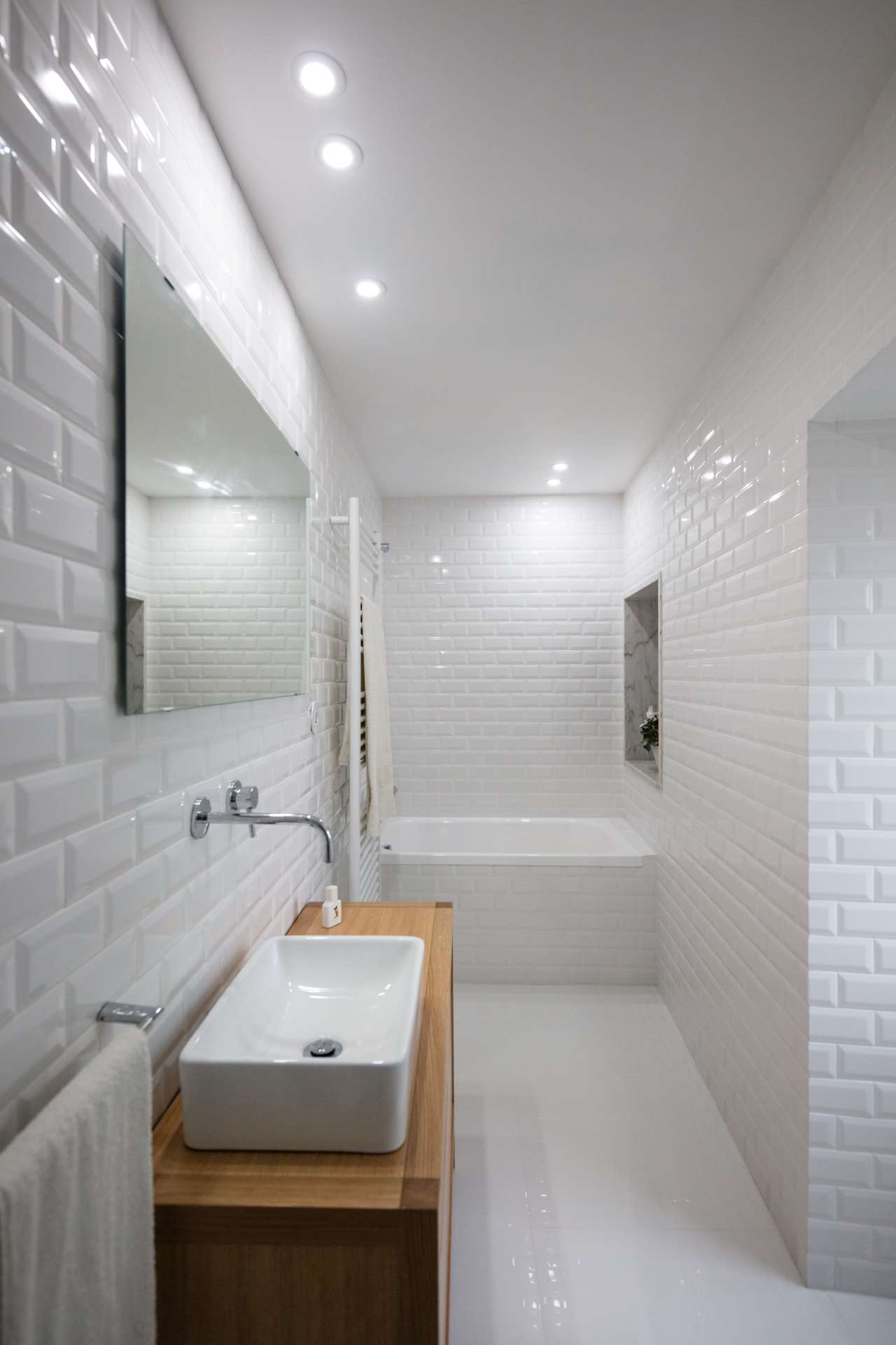 The bathroom is fully done in white, with chic tiles, a wooden vanity and a built in bathtub