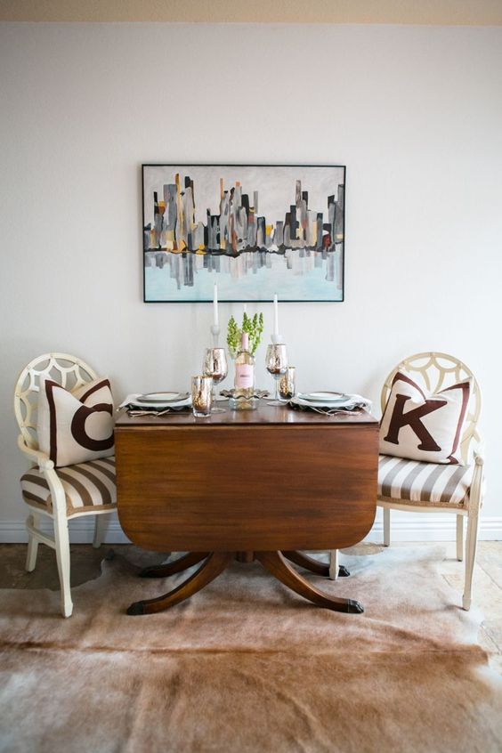 a drop leaf wooden dining table on catchy curved legs and white vintage chairs make up a stylish dining nook