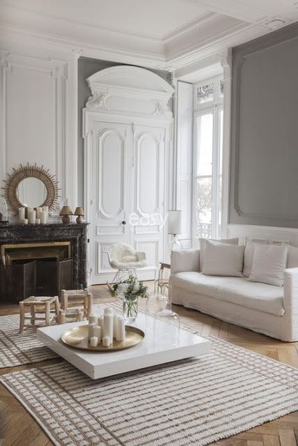 A neutral Parisian living room with light colored wood parquet floors that are covered with striped rugs