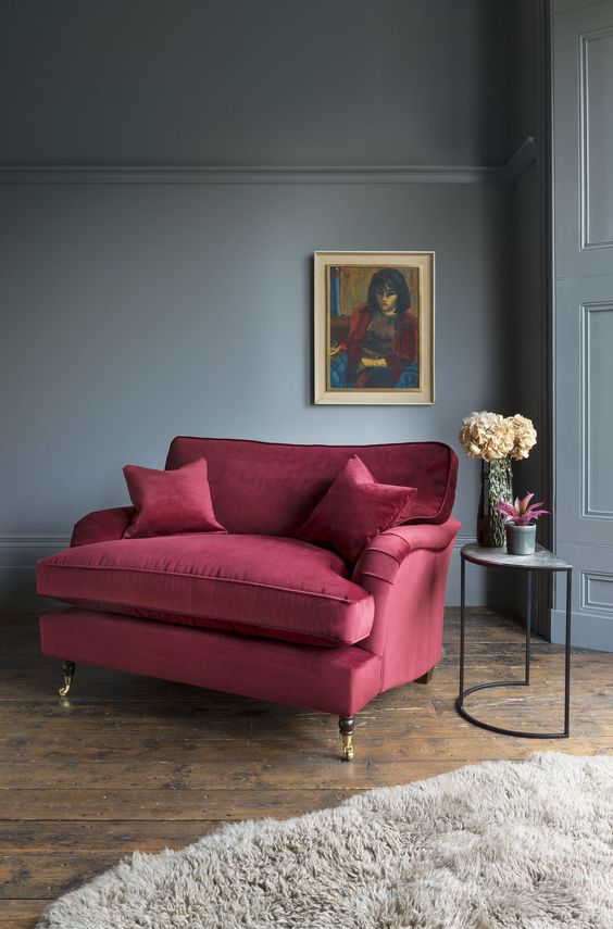 a moody living room with a burgundy loveseat and pillows, a grey faux fur rug for polishing the look