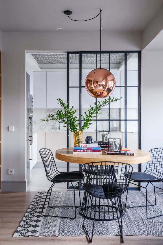 a stylish dining space with a round table on a metal base and matching black metal chairs plus a copper pendant lamp