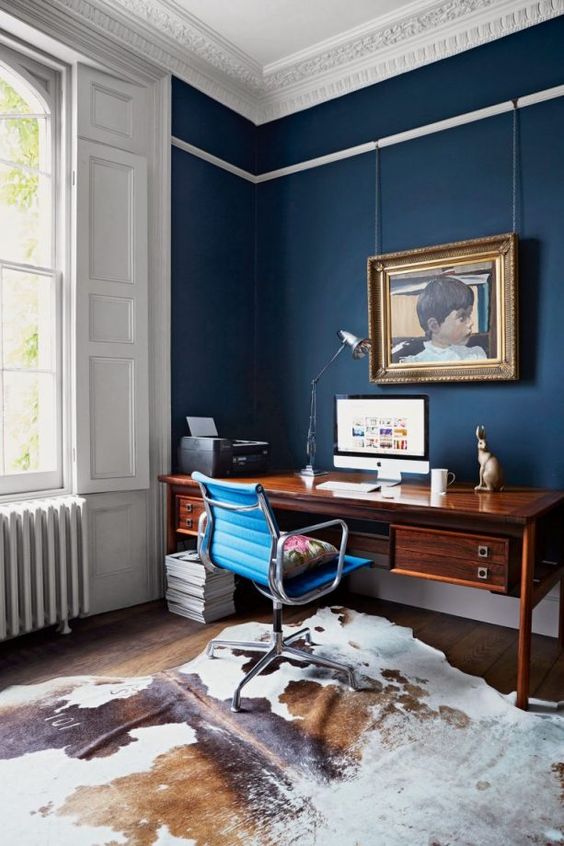 a stylish home office with navy walls, stucco, a vintage wooden desk and an animal skin rug