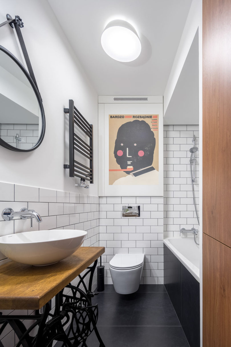 The bathroom is done in black and white, with an artwork, a unique vanity of a Zinger sewing machine and subway tiles